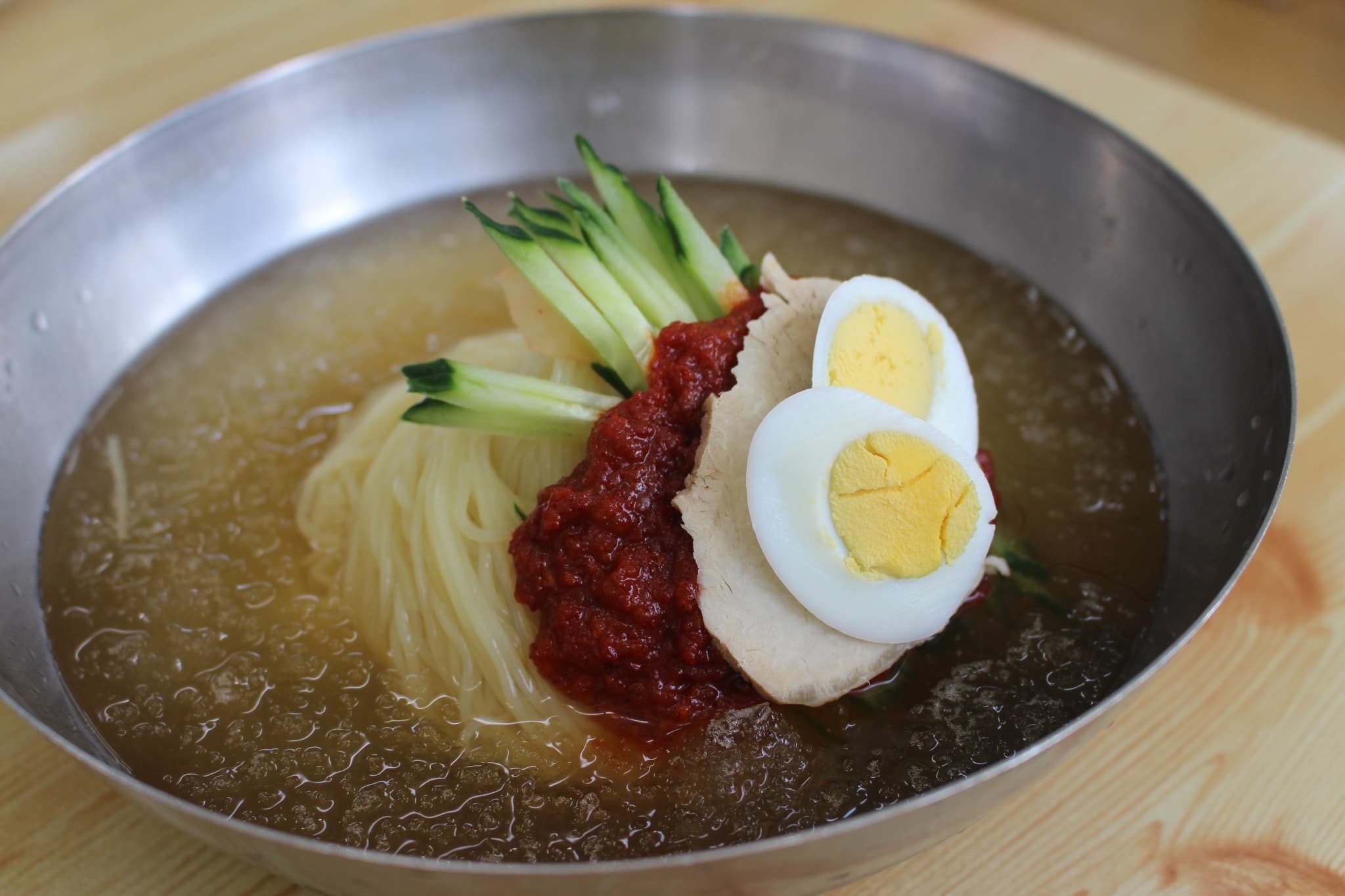 A bowl of Busan milmyeon with cold broth, noodles, egg, and red sauce